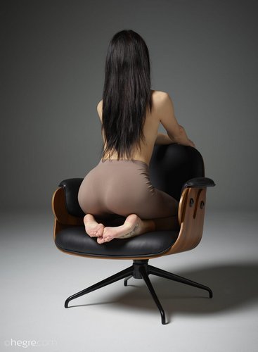 Молодая брюнетка в лосинах светит красивой попкой в кресле